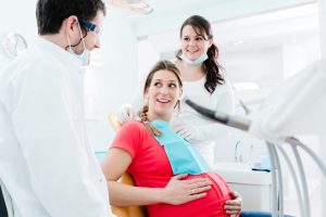 Pregnant woman sitting in dentist chair with dentist and dental nurse